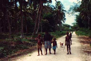 A ni-Vanuatu woman and her children walk along a coral-surfaced road.